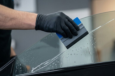 Foliowanie szyb samochodowych - mechanik nakłada folię ochronną na boczną szybę samochodu